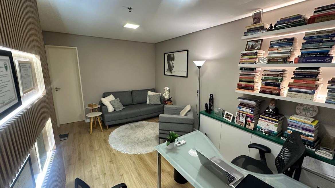 Outro ângulo da sala de consulta, com poltrona, biblioteca e diplomas